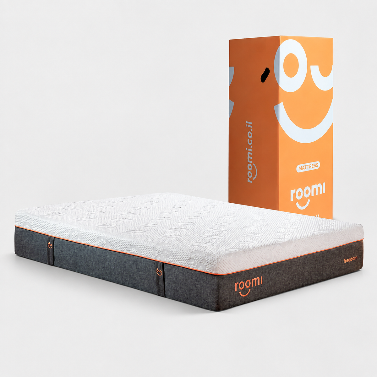 A roomi מזרן אורטופדי featuring a white top and dark gray sides is shown beside its distinctive orange and white packaging, which showcases a large smiley face and the roomi logo. For enhanced comfort, it’s ideally complemented by כריות Memory Foam.
