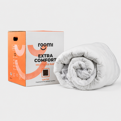A rolled-up white mattress pad sits beside an orange and white box labeled Roomi Extra Comfort Mattress Pad on a plain background, making it an ideal accessory for any מזרן אורטופדי or as a מגן מזרן to provide extra comfort and protection.