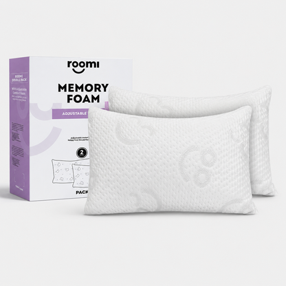 Two white כריות Memory Foam pillows are displayed in front of a purple and white box labeled Roomi Memory Foam Adjustable Pillow, which features product information and an illustration of the pillows.