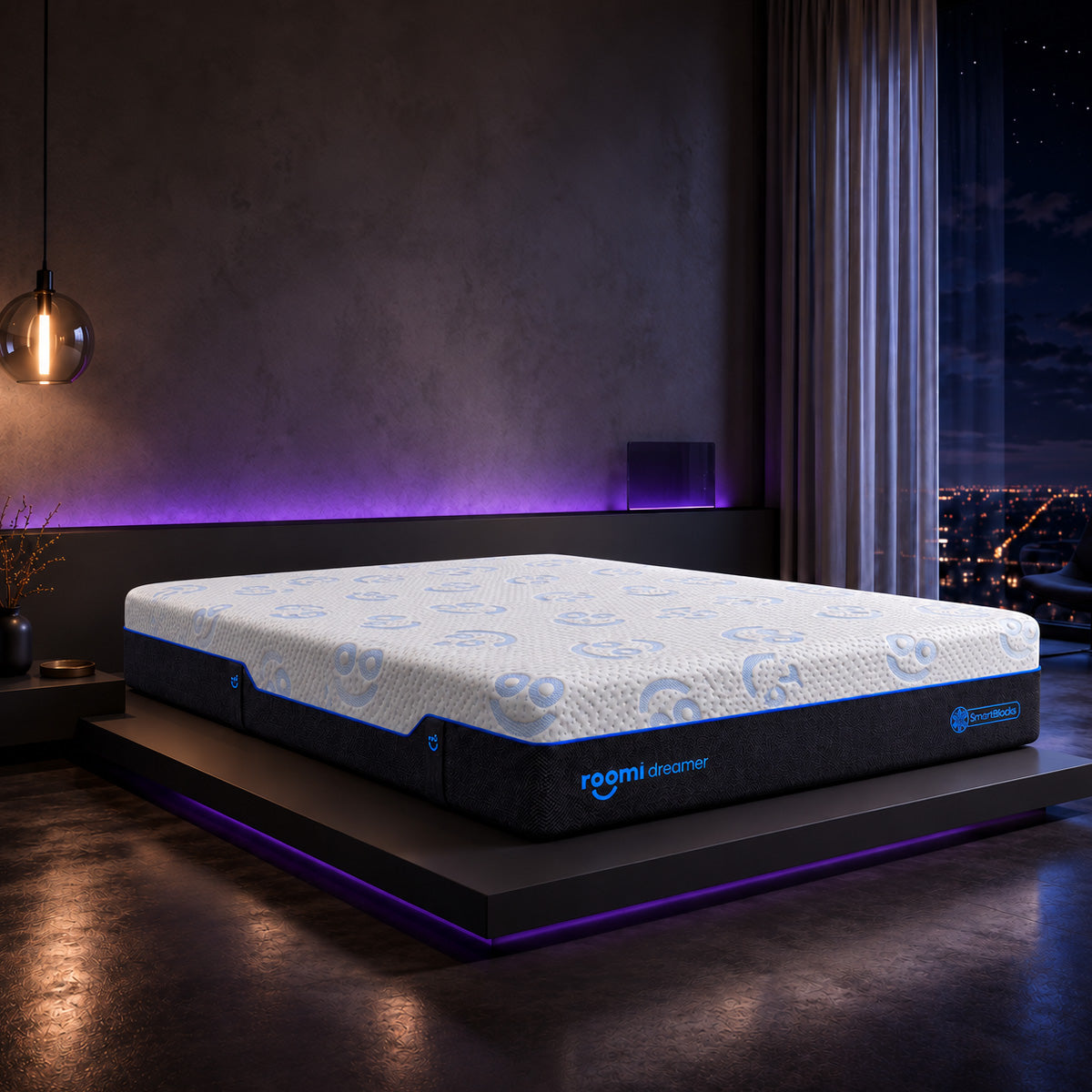 מזרן Roomi Dreamer SmartBlocks® עם חלק עליון לבן מעוטר ודפנות כהות, מונח על מיטה מודרנית בשעת לילה.